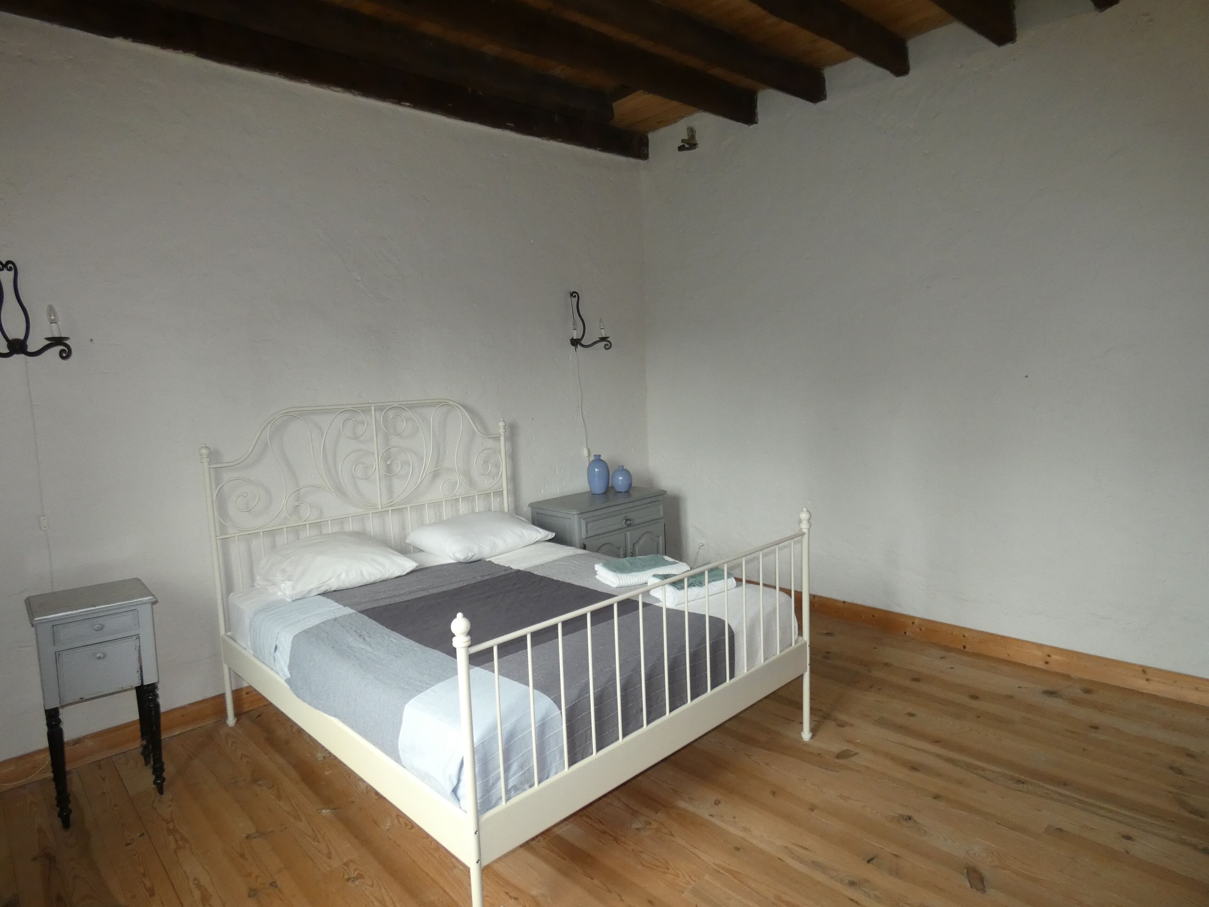 Een slaapkamer met een bed met wit metalen frame, een houten vloer en een witte wand.