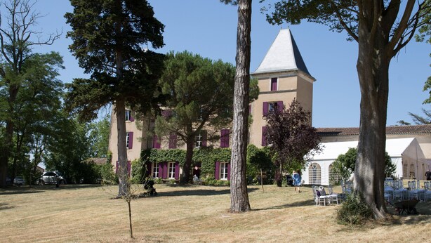 Un bâtiment doté d’une tour, entouré d’arbres et d’une zone herbeuse.
