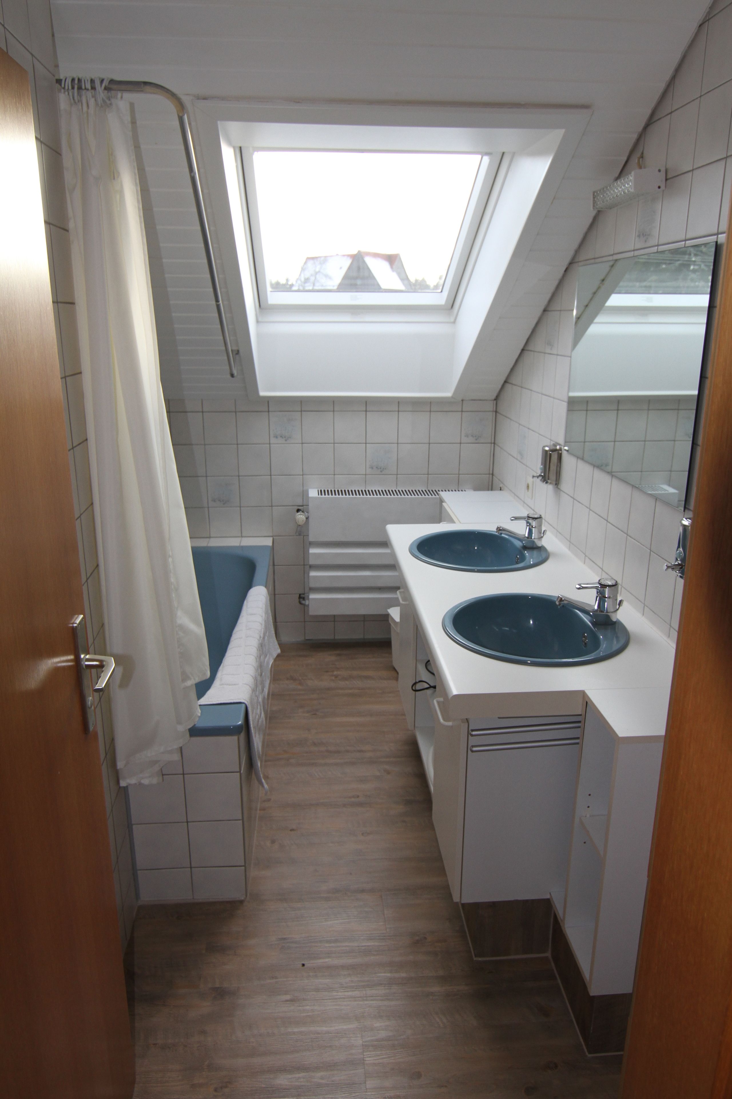 Un bagno stretto con due lavabi, una doccia e un lucernario.