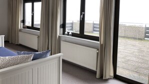 A bedroom with a bed, two windows with curtains, a radiator, and a view of the outside. - Ebnisee Apartments (Kaisersbach)
