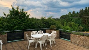 An outdoor patio with a round table and white chairs, surrounded by a gravel floor and a low stone wall. - Ebnisee Apartments (Kaisersbach)
