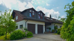A two-story house with a sloped roof, large windows, and a garage. - Ebnisee Apartments (Kaisersbach)