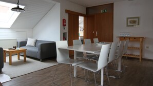 A modern living room with a dining area, a grey sofa, a wooden table, and a ceiling fan. - Ebnisee Apartments (Kaisersbach)