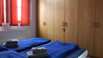 A bedroom with two beds, wooden wardrobe, red curtains, and a radiator.