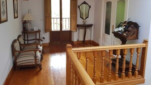 Ein großzügiges Wohnzimmer mit einer Holztreppe, einem Klavier, einem Spiegel und einer Tür zu einem anderen Raum.