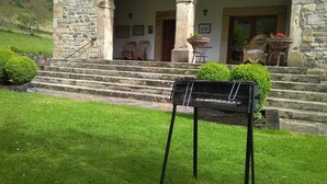 Ein Steinhaus mit überdachter Veranda, Stufen zum Eingang und einem Grill vor der Fassade.