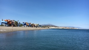 Ein Küstenort mit bunten Gebäuden entlang des Strandes, einem klaren blauen Himmel und ruhiger See.
