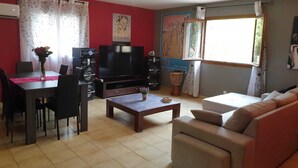 Un salon comprenant un téléviseur, des haut-parleurs, une table basse, un canapé et un coin repas avec des chaises et une table.
