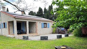 Une maison en pierre avec un toit en tuiles, une véranda et une cour couverte d’herbe.