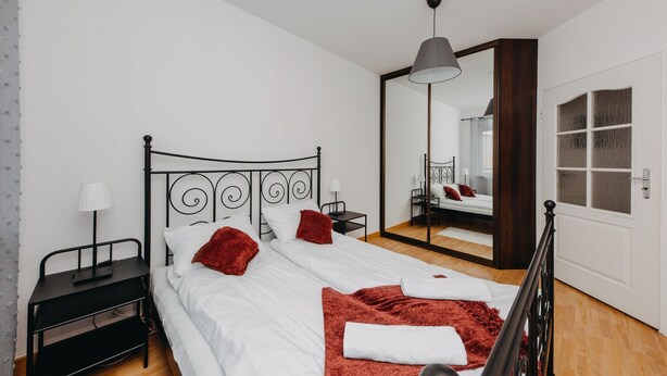 A bedroom with a bed, a nightstand, a lamp, a mirror, and a door. - ShortStayPoland Krochmalna - B39 (Warsaw)