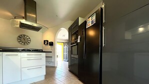 Une cuisine moderne avec un réfrigérateur en acier inoxydable, des meubles blancs et une horloge au mur.
