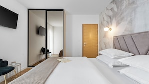 Une chambre moderne avec un grand lit, un téléviseur à écran plat fixé au mur, une porte en bois et un luminaire fixé au mur.