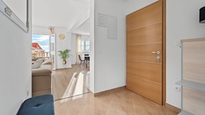 Un salon moderne avec un canapé, une table basse et un coin repas avec des chaises. On y trouve une porte en bois et une petite étagère.