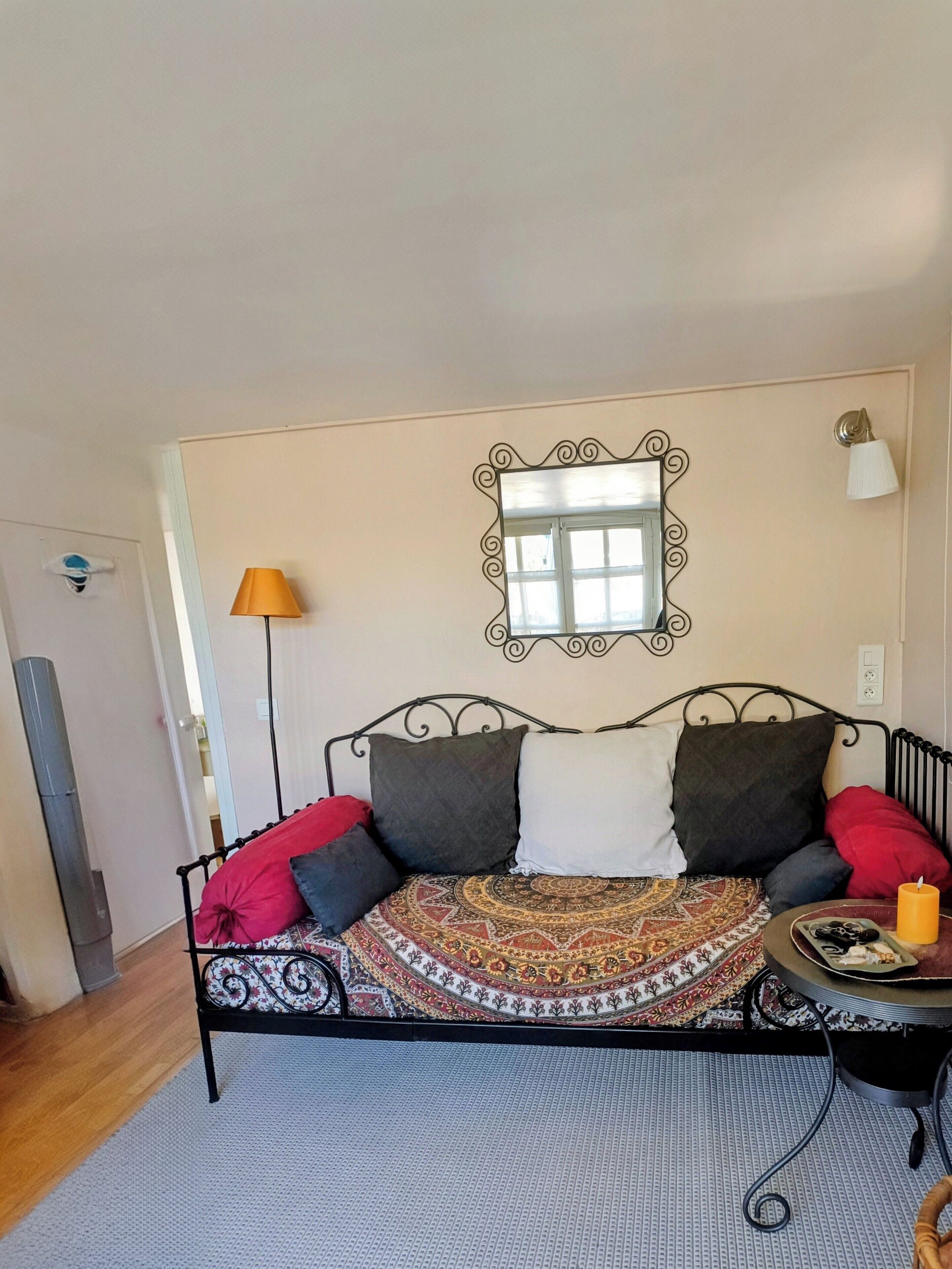 A room with a bed, a patterned rug, a wall-mounted mirror, and a lamp.