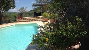 A swimming pool with a garden area, a pergola, and a view of the surrounding landscape.