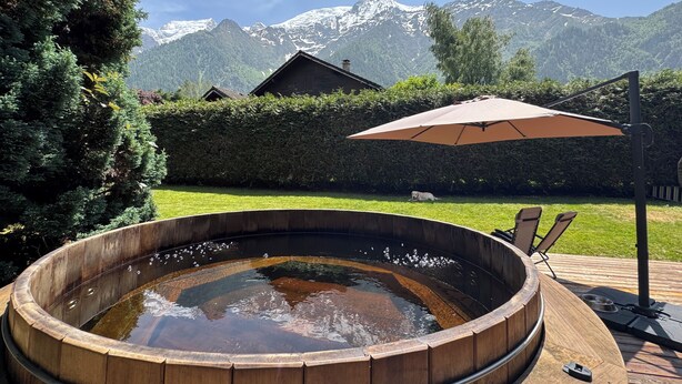 A wooden hot tub with a view of snow-capped mountains in the background.
