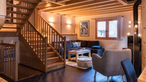 A wooden staircase leading to a living area with a sofa, ottoman, and a dining table.