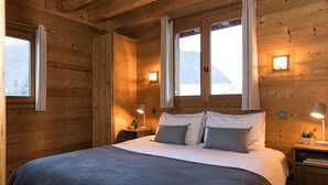 A wooden cabin bedroom with a large bed, two bedside tables with lamps, and a window with curtains.