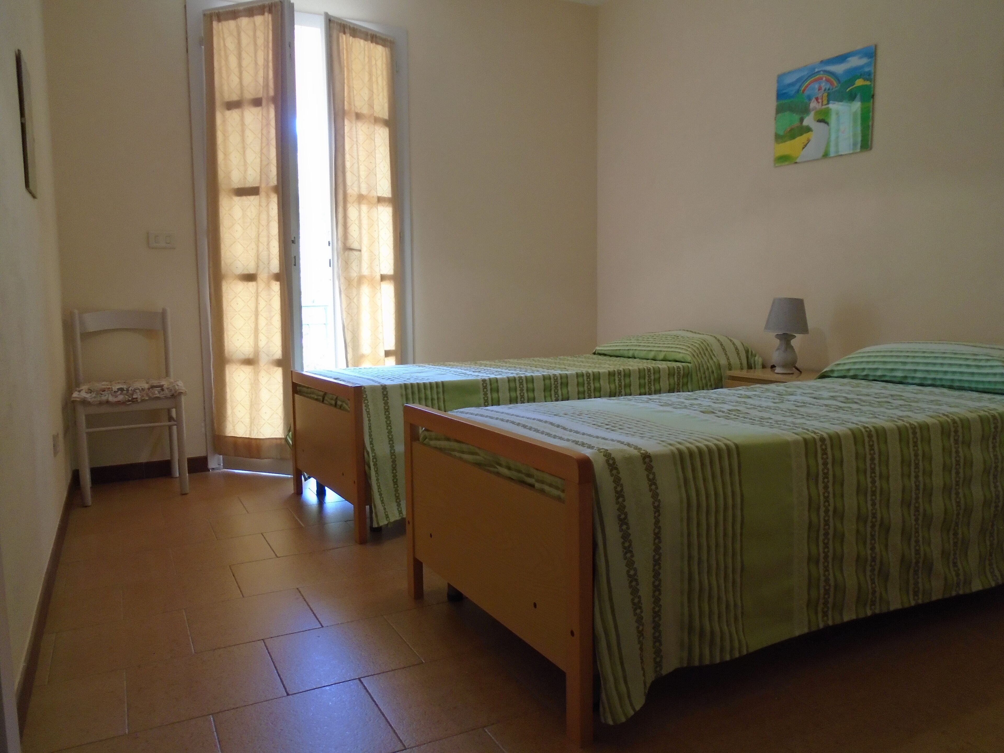 A room with two wooden beds, a chair, and a painting on the wall.