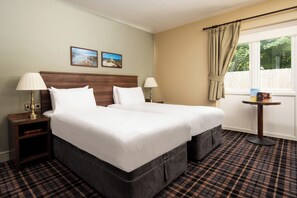 A double bed with a wooden headboard, two bedside tables with lamps, a small round table, and a window with curtains.