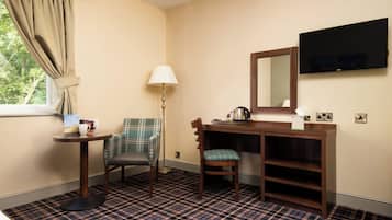 Une chambre d’hôtel avec un tapis à carreaux, un bureau avec un miroir, un téléviseur fixé au mur et une fenêtre avec des rideaux.