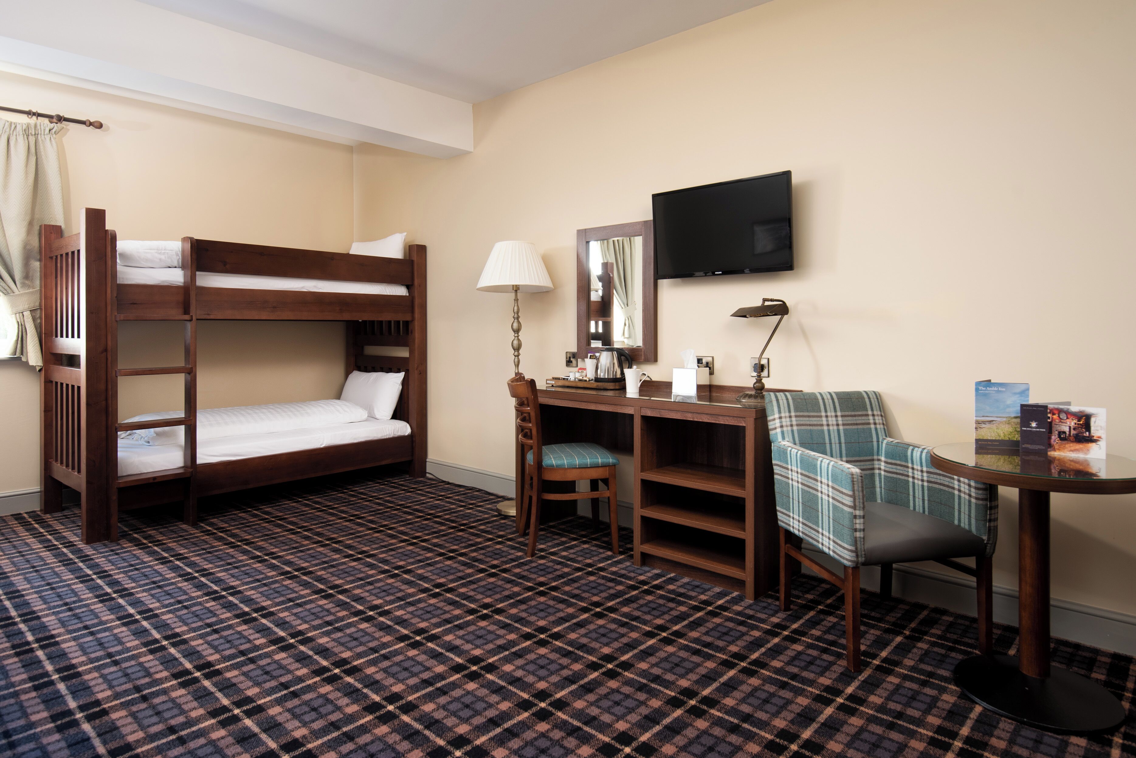 Hotelkamer met een stapelbed, een bureau met stoel, een lamp, een televisie en een kamerbreed tapijt met een patroon.