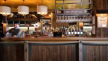 A bar area with a wooden counter, hanging wine glasses, and a sign reading "AMBLE IN COCKTAILS".