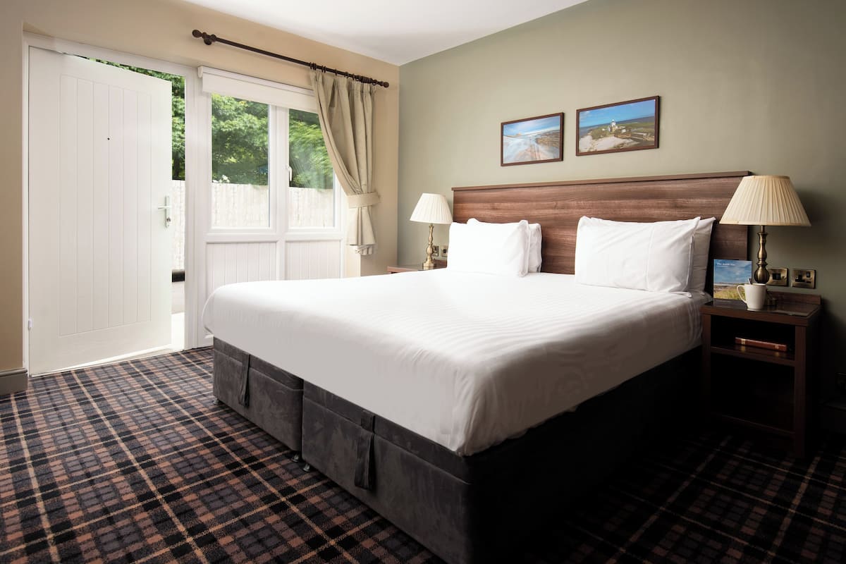A hotel room with a large bed, two bedside tables, a nightstand, a window with curtains, and two wall-mounted pictures.