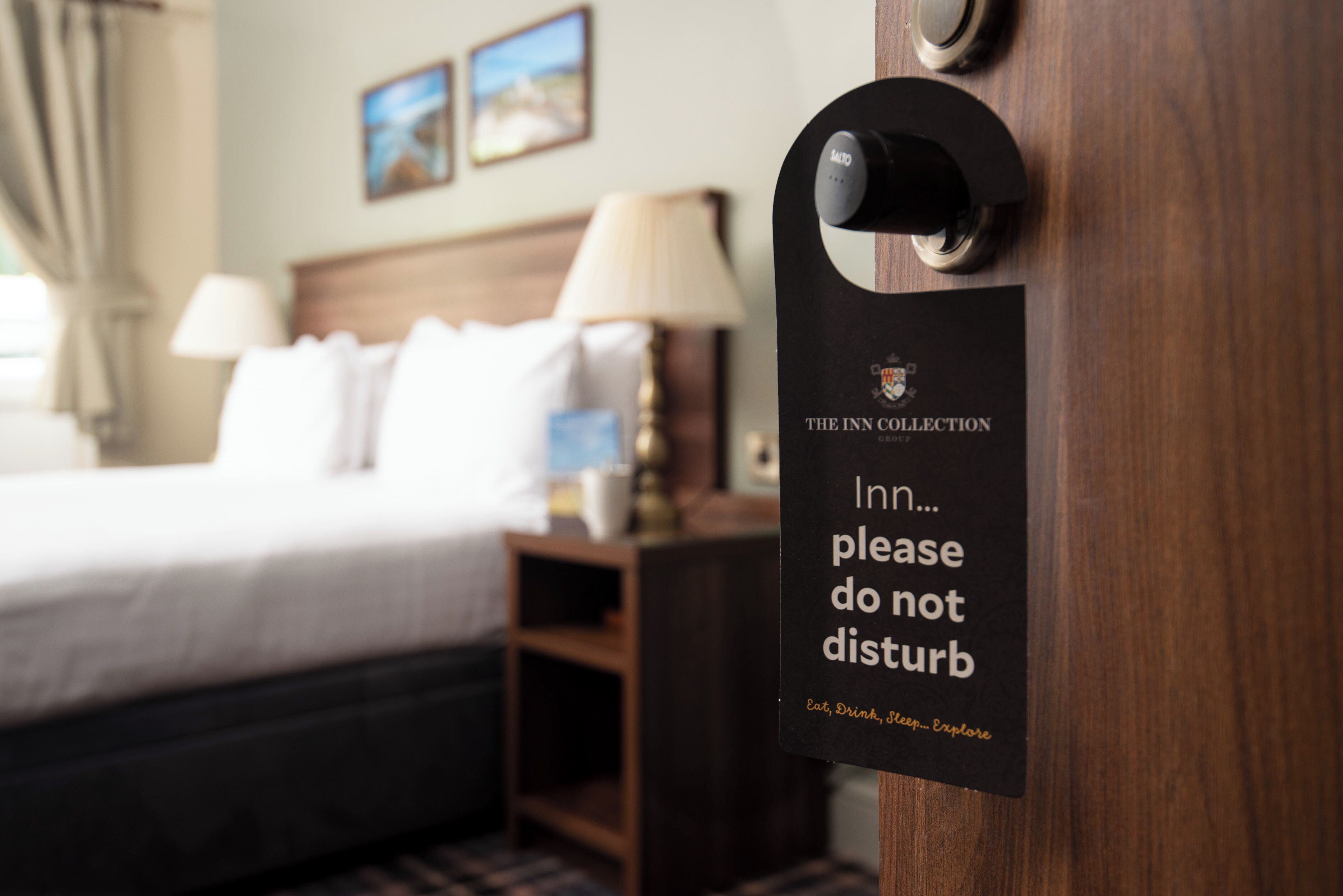 Una habitación de hotel con una cama, una mesita de noche, una lámpara y un cartel en la puerta que dice 'The Inn Collection, por favor no molestar'.