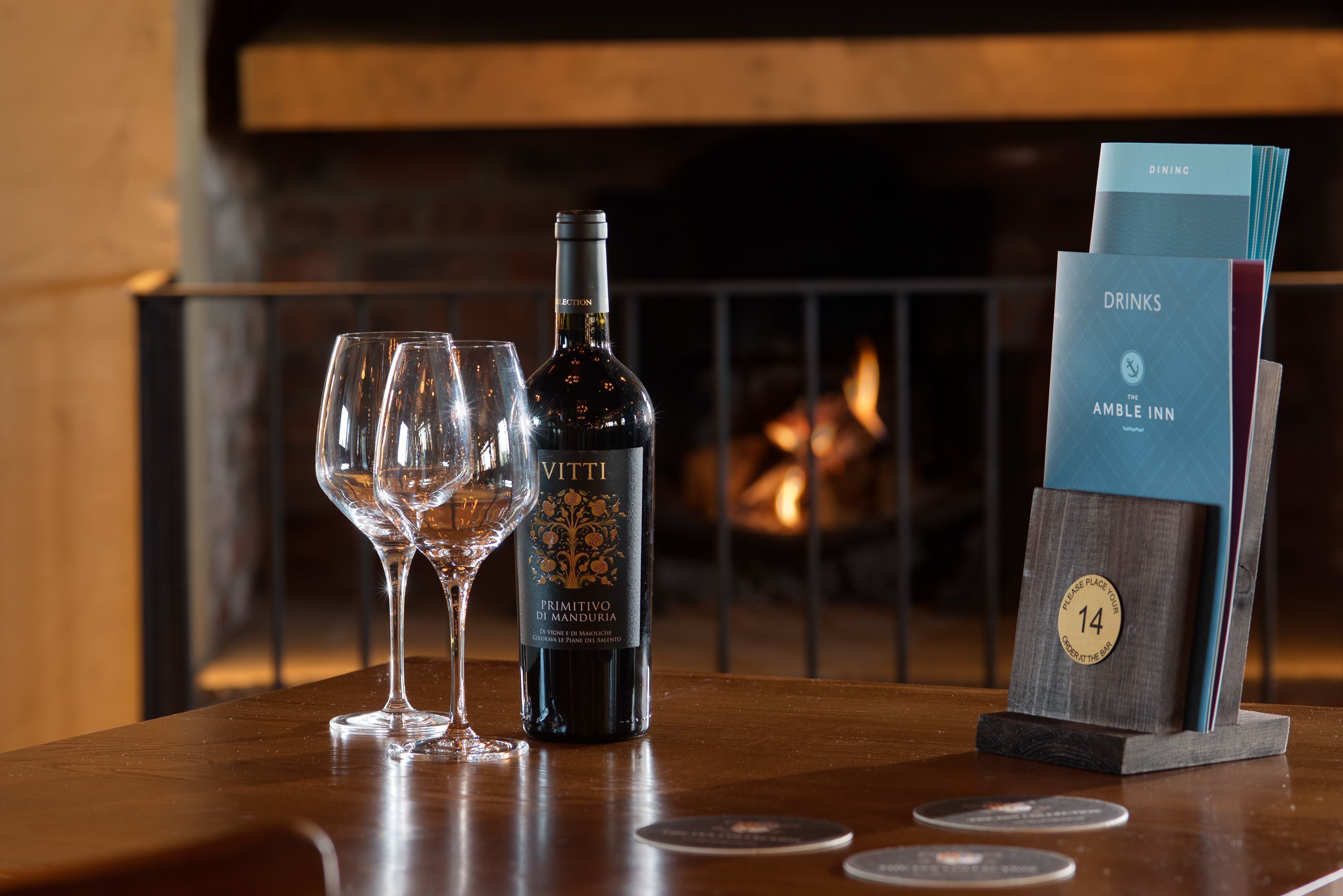 A table with a bottle of Vitti wine, two glasses, and a menu stand with a placemat labeled "14".