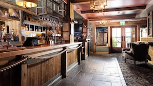 Uma área de bar com balcões de madeira, copos de vinho pendurados e piso de pedra.