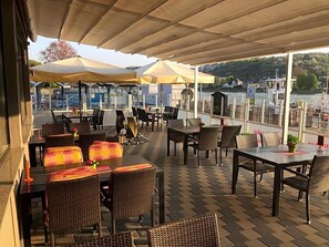 An outdoor patio with tables and chairs, umbrellas, and a view of the water.