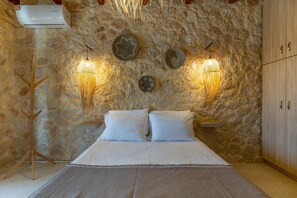 A bedroom with a stone wall, a bed with white linens, two wall-mounted lamps, and a wooden wardrobe.