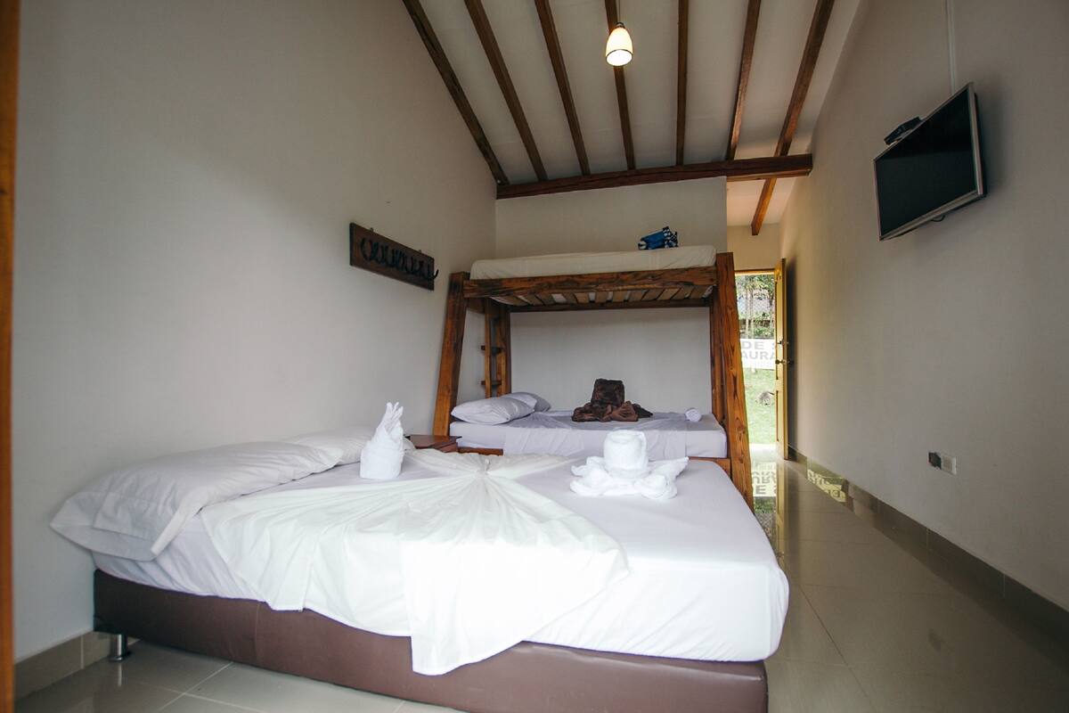 Una habitación de hotel con una cama litera, una cama doble y un televisor en la pared.
