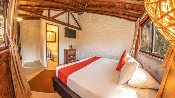 Un dormitorio con techo de madera, cama con ropa de cama blanca y roja, mesita de noche y ventana con cortinas.