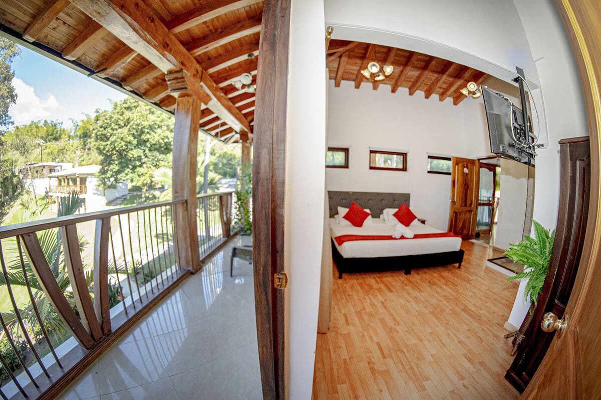 Un dormitorio con una cama grande, piso de madera y un balcón con barandilla.