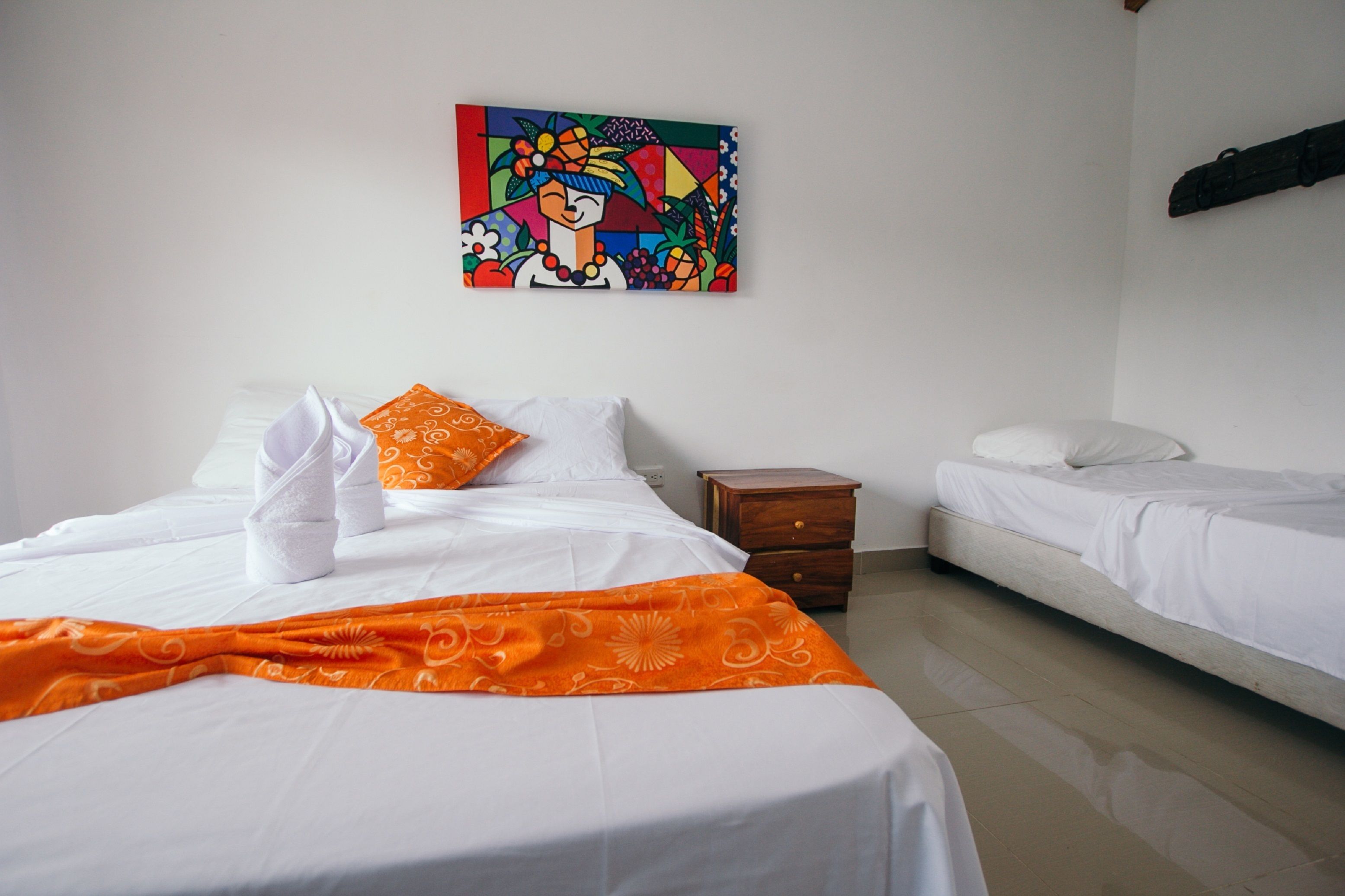 A hotel room with two beds, a wooden nightstand, and a colorful abstract painting on the wall.