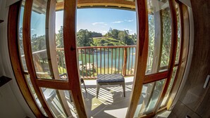 Vista panorámica desde un balcón con barandilla de madera, con vistas a un lago y paisaje verde.
