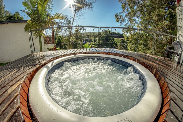A hot tub surrounded by a wooden deck with a view of trees and a clear sky. - Mansion by Bernalo Hotels (Guatapé)