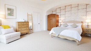 Ein Schlafzimmer mit Bett, Schminktisch, Nachttisch, Lampe und einem gerahmten Bild an der Wand.