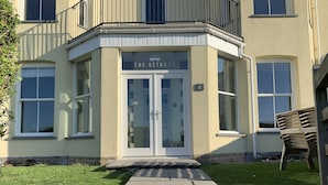 Ein Eckgebäude mit Glastür, einer kleinen Außenbestuhlung und einem gepflasterten Weg zum Eingang.