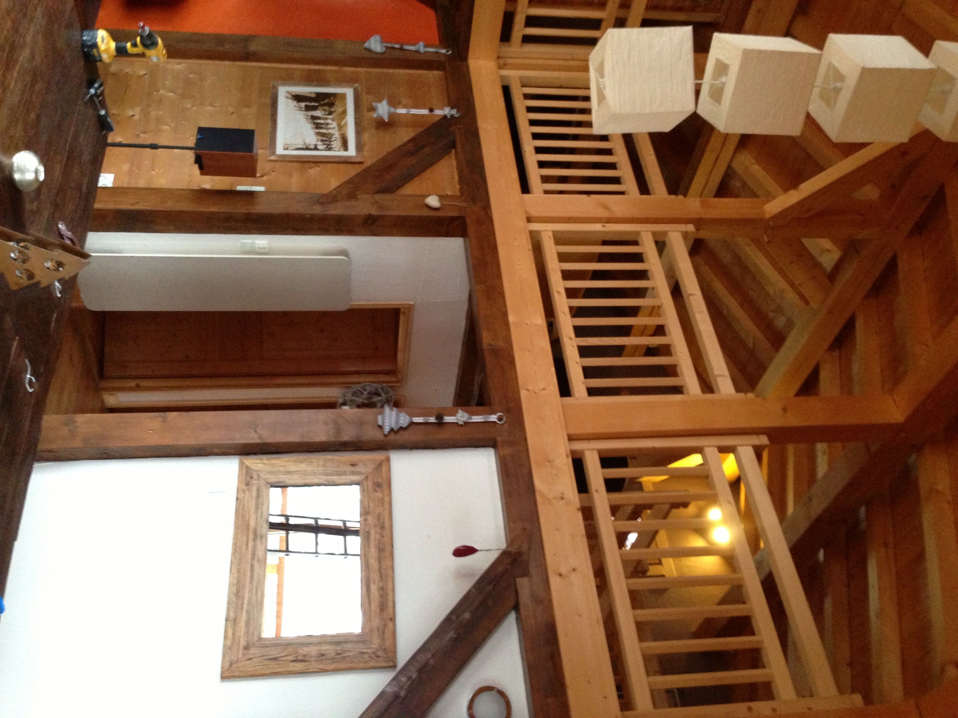 Um quarto com pé direito alto, vigas de madeira aparentes, uma janela grande e uma escada de madeira.