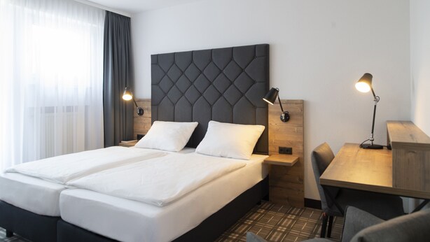 Habitación de hotel con cama doble, dos mesitas de noche con lámparas, un escritorio de madera y una silla.