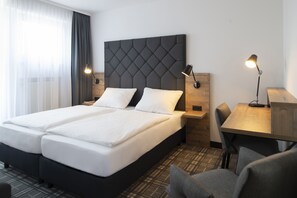 A hotel room with a double bed, two bedside tables with lamps, a wooden desk, and a chair. - Platzhirsch Hotel (Bonn)