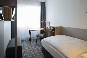 A hotel room with a bed, a desk, a chair, a wardrobe, and a window with curtains. - Platzhirsch Hotel (Bonn)