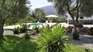 Un espace piscine doté d’un coin salon abrité, entouré de verdure et offrant une vue sur les collines.