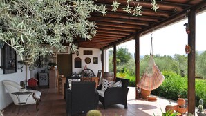 Un patio couvert aménagé avec des meubles en osier, des plantes en pot et un fauteuil suspendu.