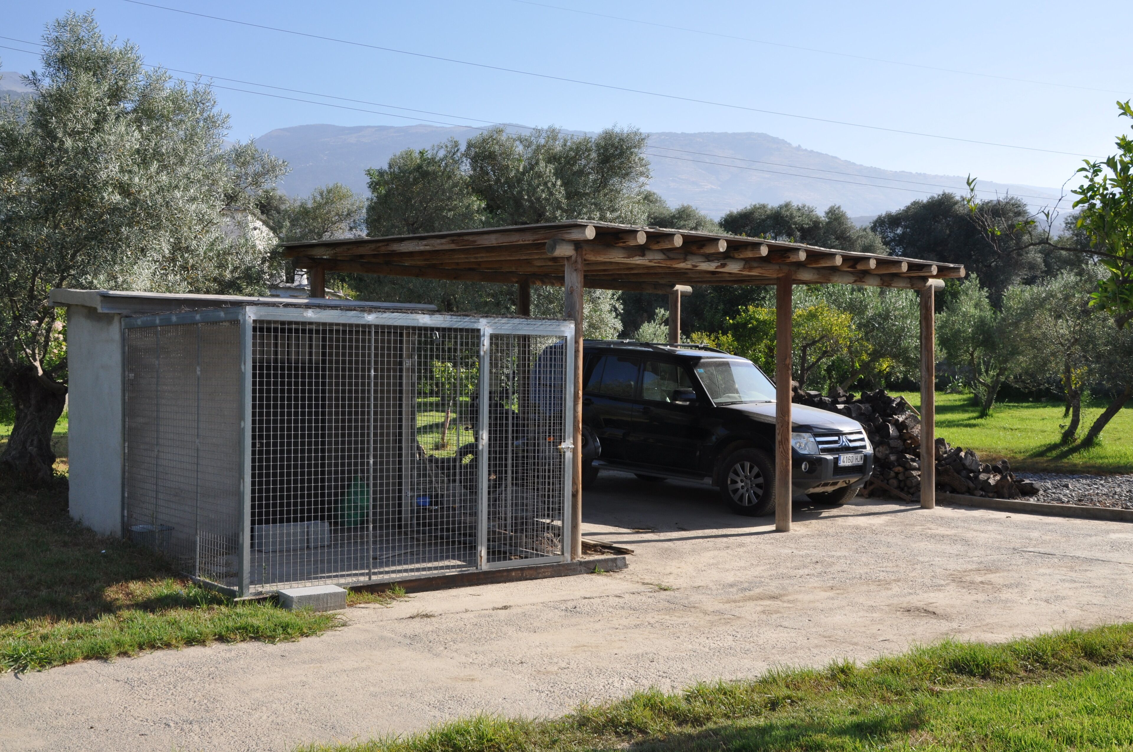 A covered outdoor area with a car and a fenced enclosure.