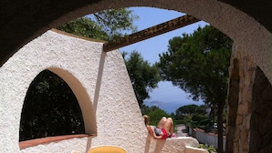Een terras buiten met een tafel en stoelen, een stenen muur en uitzicht op zee.