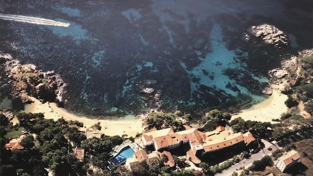 Luchtbeeld van Camí de Ronda, met een kustlandschap, een strand, rotsformaties en een groep gebouwen met terracotta daken.